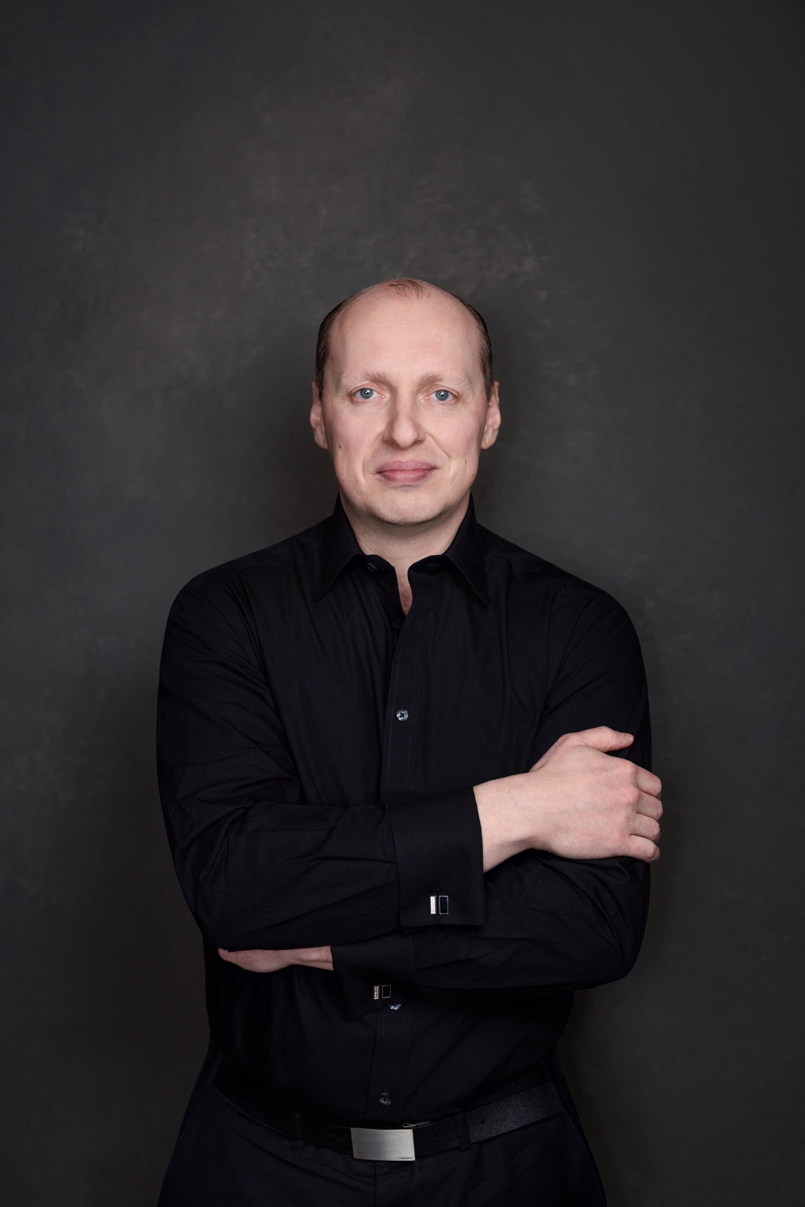 Yuriy Demidko in a black shirt, arms crossed, against a dark studio backdrop